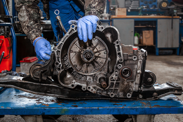 A close-up of a young man repairman in a working uniform of cars is repairing an automatic gearbox of a used car in an auto repair shop
